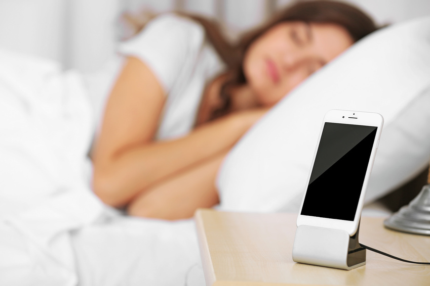 Beautiful young woman waking up with mobile alarm clock